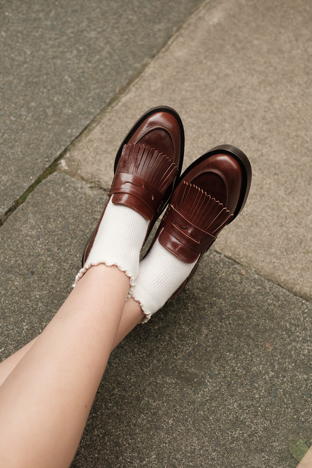 Femme posant dans une rue de Londres avec une veste en laine brune et des chaussures Pied de Biche.