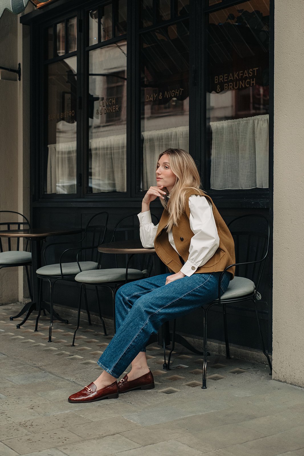 Femme assise dans un café à Londres portant des mocassins marron Pied de Biche.