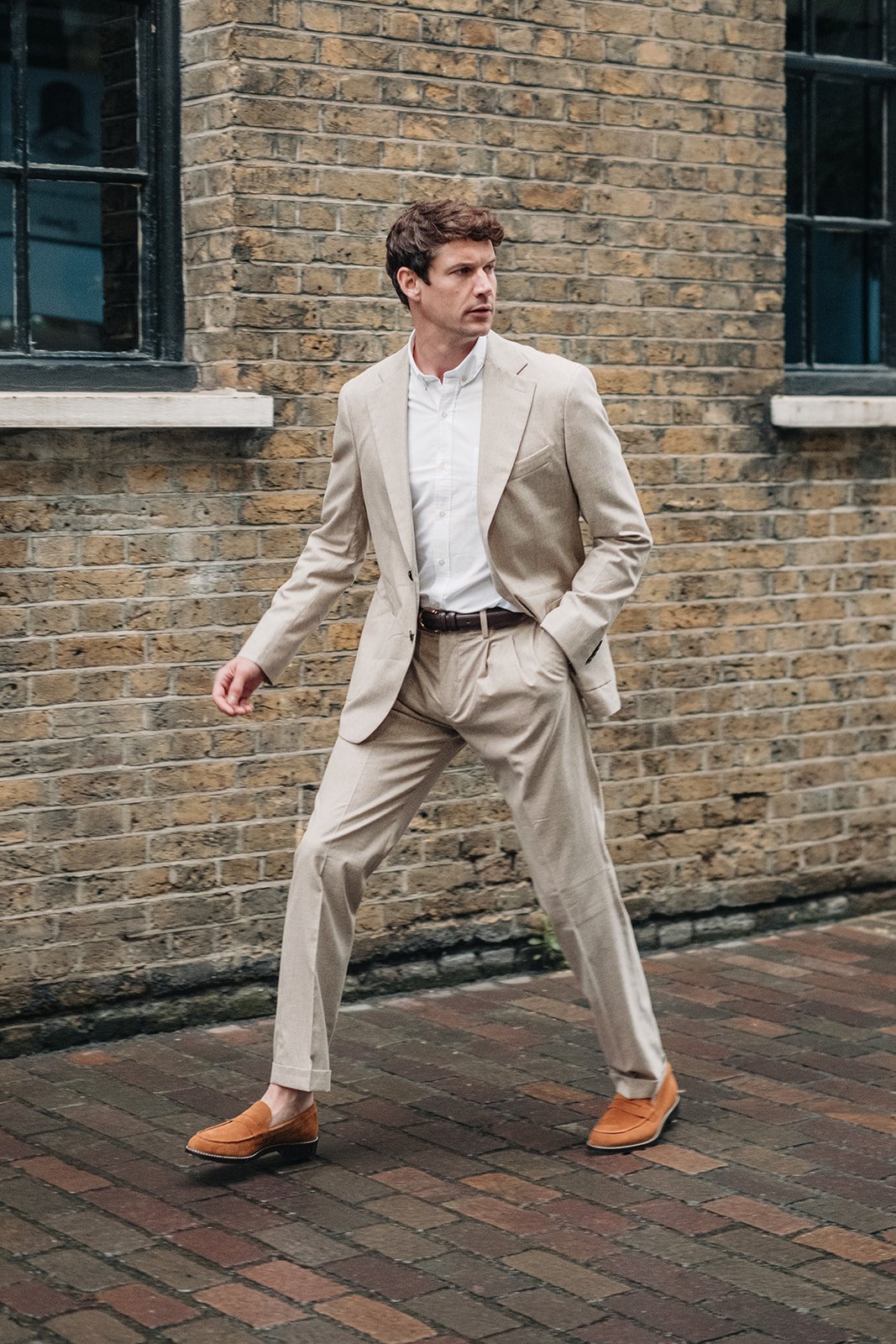 Homme en costume beige marchant dans une rue pavée à Londres pour une séance photo de mode.