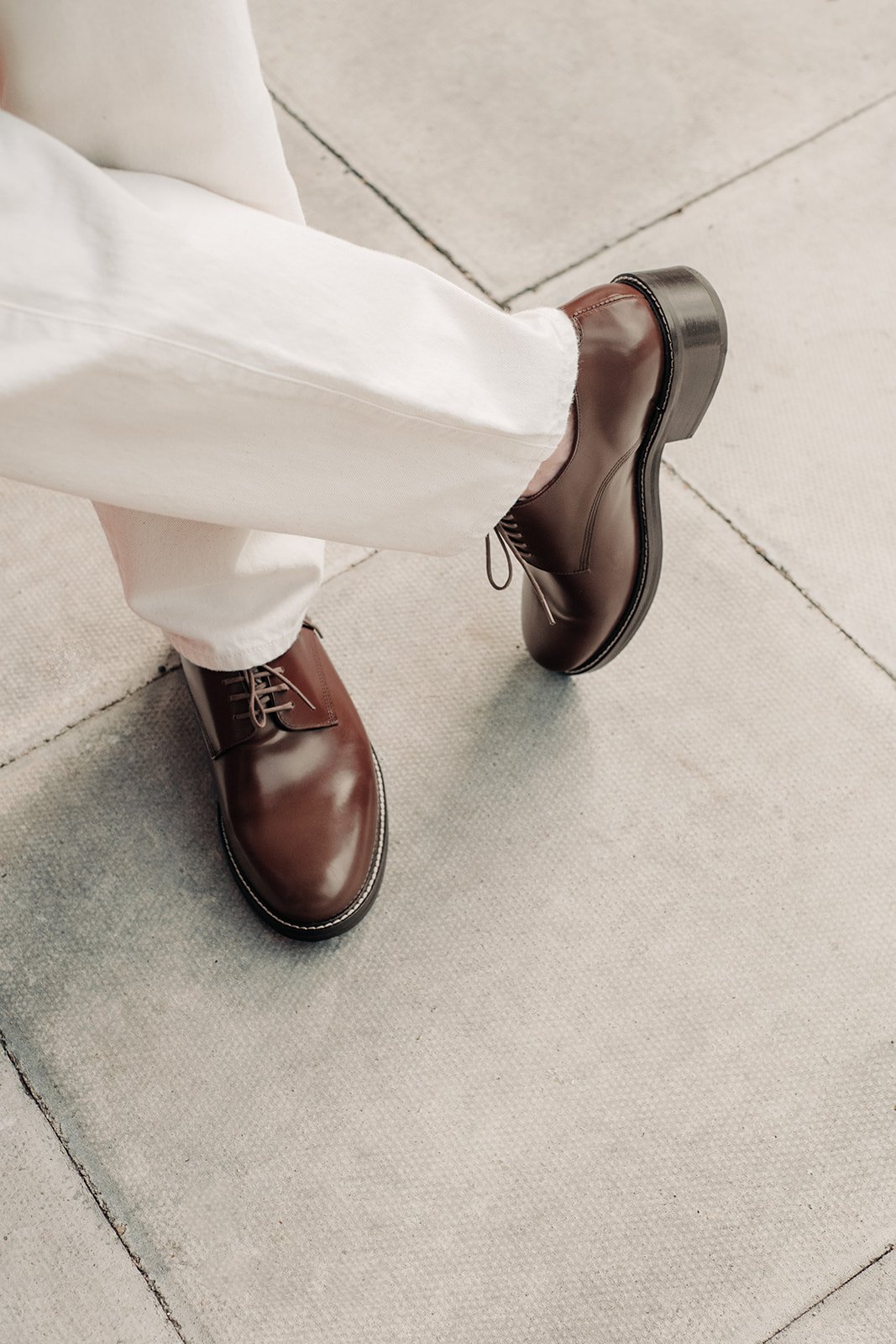 Homme en costume beige, posant élégamment devant un mur de briques dans les rues de Londres.